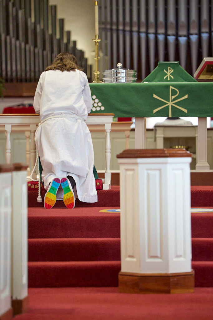 Pastor kneeling at altar with rainbow colors on the soles of her shoes.